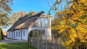 Una casa tradizionale con tetto di paglia, facciata bianca e recinzione in legno.