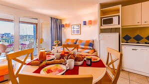 Quarto com uma mesa de jantar posta para o café da manhã, um sofá com almofadas laranja e azuis, micro-ondas e lava-louças.