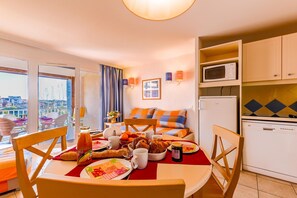 Ein Zimmer mit Esstisch, gedecktem Frühstücksservice, einer Couch mit orange- und blauen Kissen, einer Mikrowelle und einem Geschirrspüler.