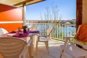 Ein Balkon mit Esstisch, weißen Plastikstühlen und Blick auf ein Gewässer sowie Gebäude.