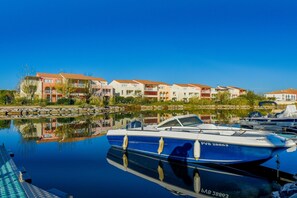 Ein Yachthafen mit vertäuten Booten, ein ruhiger See spiegelt Gebäude wider und ein klarer, blauer Himmel.