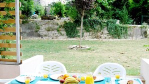 Ein Essbereich im Freien mit einem für das Frühstück gedeckten Tisch, inklusive Tellern, Besteck und einer Obstschale.