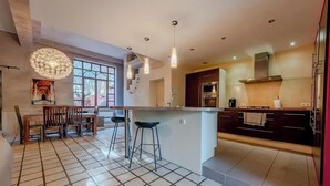 A modern kitchen with a central island, bar stools, pendant lighting, and a large window. - Villa avec piscine 8 pers proche Perpignan (Saleilles)