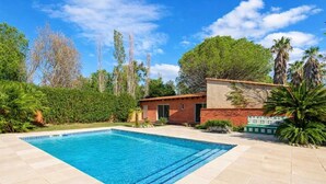 A swimming pool with a tiled deck, a small building with a red roof, and surrounding greenery. - Villa avec piscine 8 pers proche Perpignan (Saleilles)