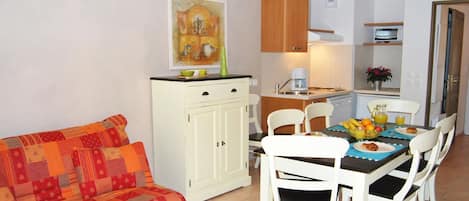 A dining area with a table set for four, a white cabinet, and a sofa with a colorful cushion.