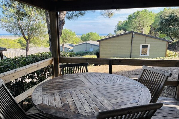 A wooden deck with a round table and chairs, overlooking a residential area with houses and trees.