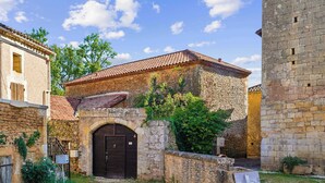 A stone building with a tiled roof, a central arched doorway, and a small garden area.