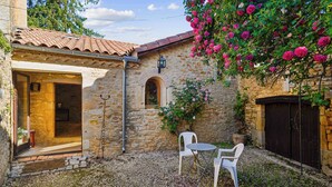 A stone building with a tiled roof, a doorway, and a small table with two chairs.