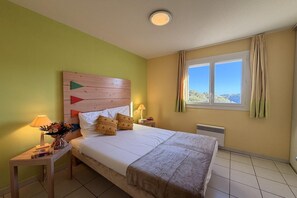 Ein Hotelzimmer mit Bett, Nachttisch mit Lampe, Fenster mit Vorhängen und Blick nach außen.