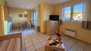 A room with a bed, a dining table with chairs, a TV, a radiator, and a window with curtains. - Mediterranean Sea View Escape for 6 (Cerbère)