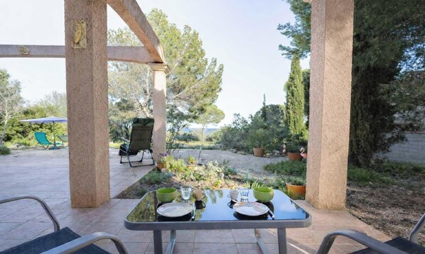 An outdoor patio with a table set for dining, surrounded by chairs, and a view of the garden. - La Terrasse d'Azur – Vue Mer, Jardin & Parking (La Palme)