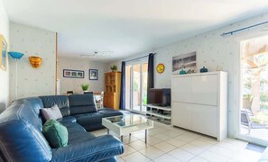 A living room with a black leather sofa, a glass coffee table, a TV, and a cabinet. - La Terrasse d'Azur – Vue Mer, Jardin & Parking (La Palme)