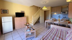 A compact living space with a kitchenette, a dining area, a bed, a TV, and a staircase. - Hillside Mediterranean Stay for 6 (Cerbère)