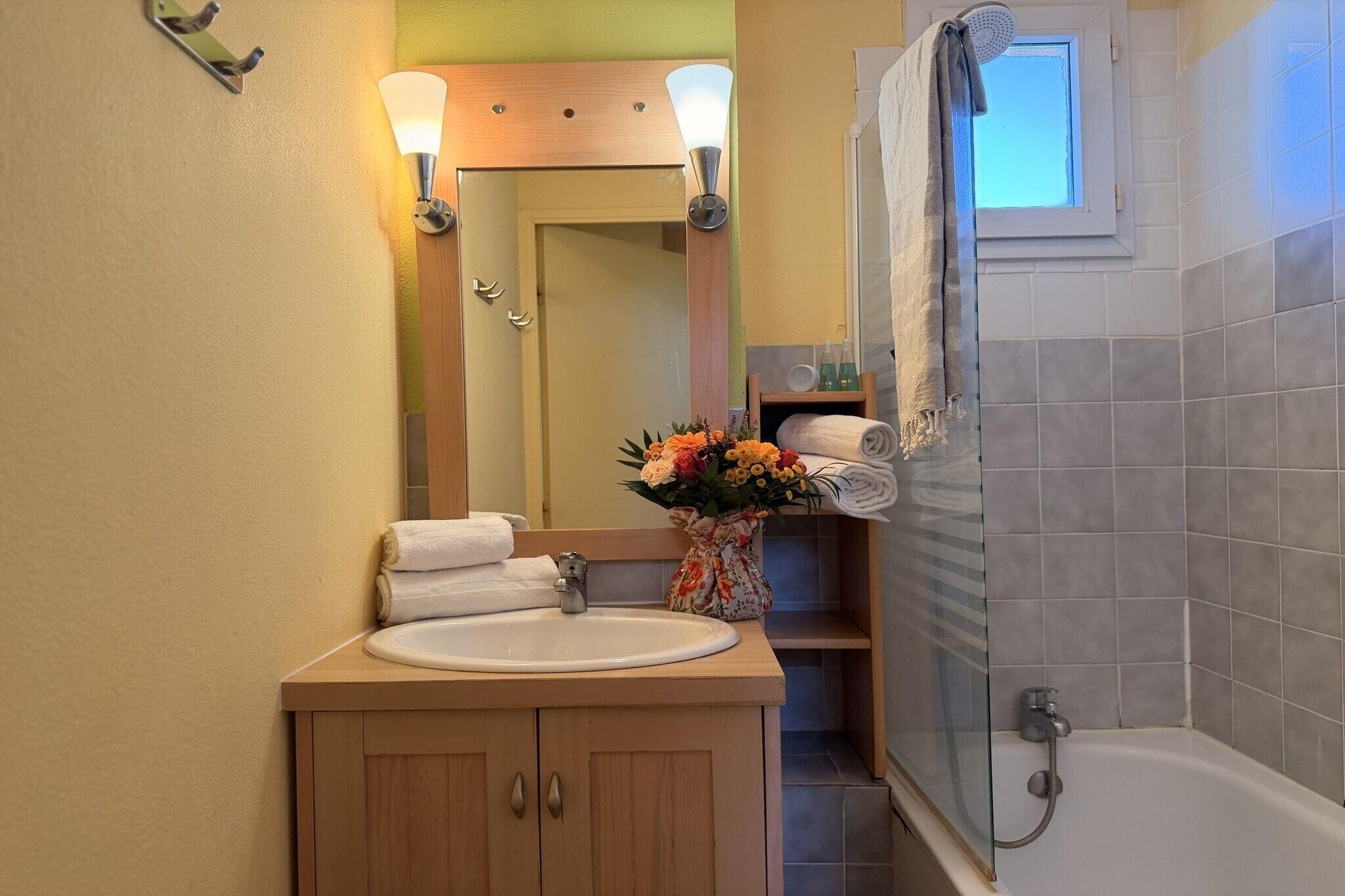 Een badkamer met een wastafel, spiegel, douche en een bloemenvaas.