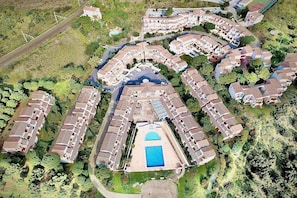 Vue aérienne d’un quartier résidentiel avec une piscine centrale, entourée de maisons à étages dotées de balcons.