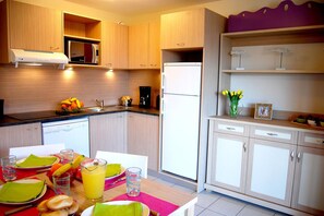Eine moderne Küche mit Holzausstattung, einer Mikrowelle, einem Kühlschrank und einem Esstisch, gedeckt mit Tellern, Gläsern und einer Obstschale.
