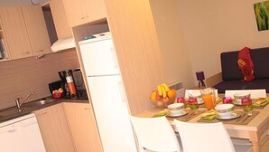 A compact kitchen with a refrigerator, a sink, and a dining area with a table set for two. - Spacious Beachside Apartment for 6 (Saint-Cyprien)