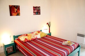 Ein Bett mit gestreifter Bettdecke, eine Nachttischlampe, ein Bilderrahmen und eine Wand-Klimaanlage.