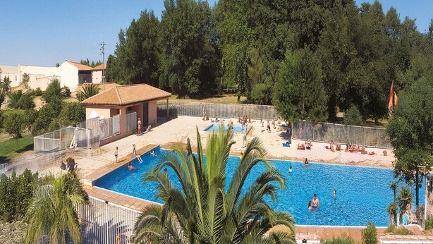 En swimmingpool med folk, et afspærret område og træer i baggrunden.