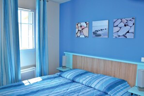 A bedroom with a bed, a nightstand, a wall-mounted lamp, and a window with curtains.