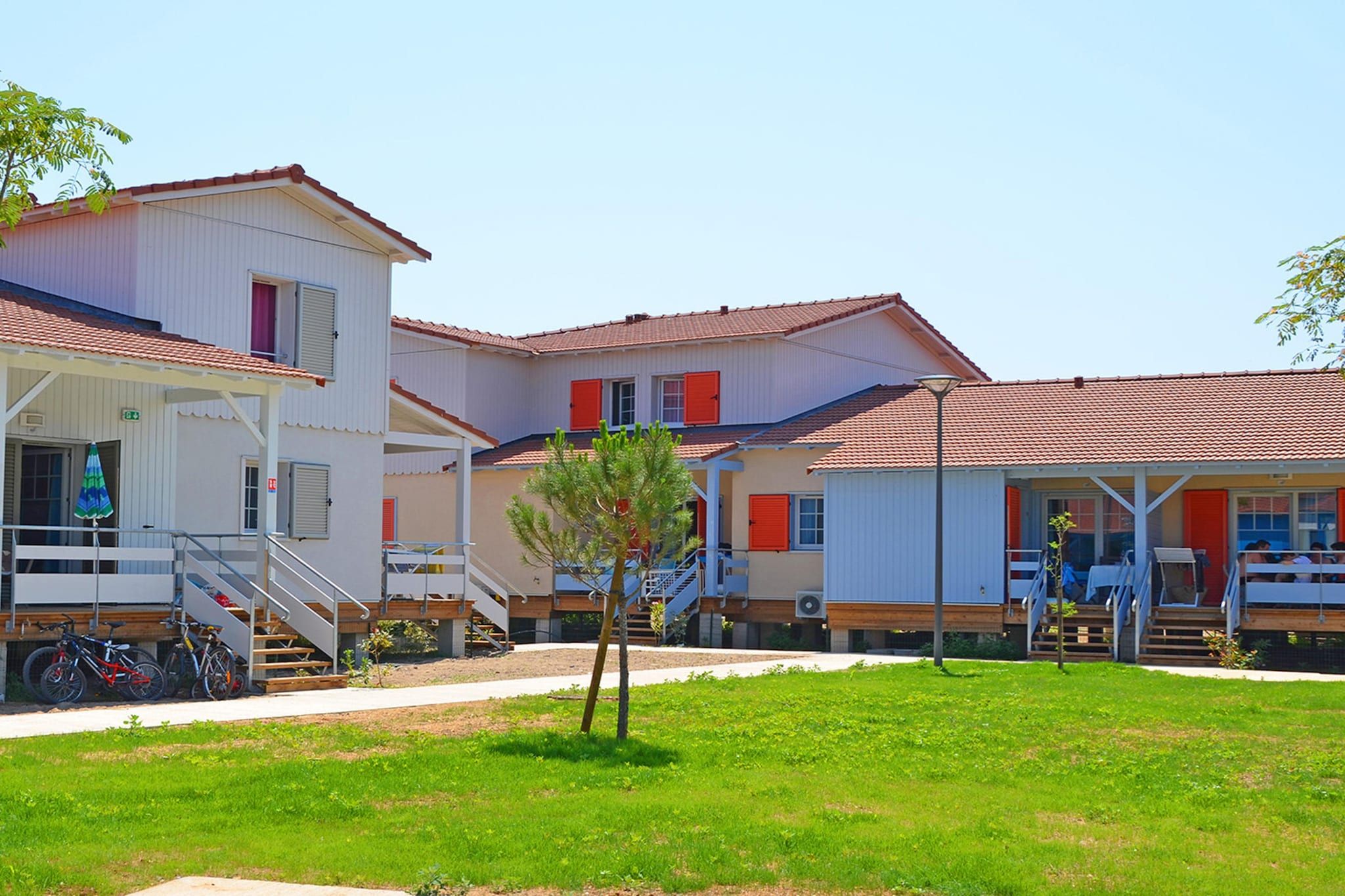 A multi-story building with a covered outdoor area, stairs, and a small tree.