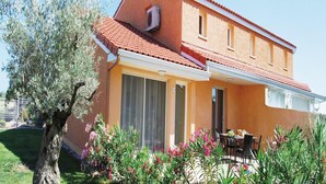 Ein zweistöckiges Gebäude mit rotem Ziegeldach, großen Fenstern und einer Terrasse mit Gartenmöbeln.