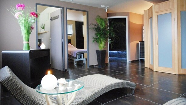 Ein modernes Hotelzimmer mit Loungebereich, einer Massageliege und einer großen Topfpflanze.