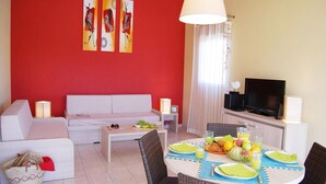 Ein Wohnzimmer mit einer Couch, einem Esstisch mit Tellern und Gläsern, einem Fernseher und Kunstwerken an der Wand.