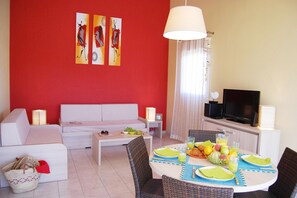 Ein Wohnzimmer mit einer Couch, einem Esstisch mit Tellern und Gläsern, einem Fernseher und Kunstwerken an der Wand.