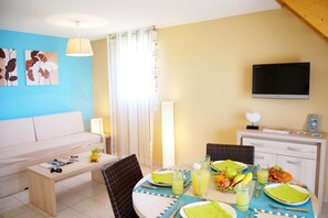 A dining area with a table set for two, a sofa, and a television mounted on the wall. - Spacious 8-guests holiday home, Torreilles (Torreilles)