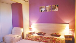 Ein Hotelzimmer mit einem Bett, einem Sessel, zwei Nachttischen und Wandbildern.