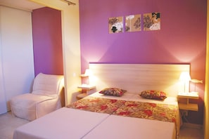 Ein Hotelzimmer mit einem Bett, einem Sessel, zwei Nachttischen und Wandbildern.