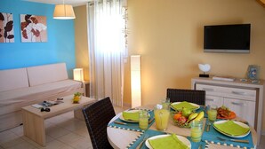 Un coin repas avec une table dressée pour deux personnes, un canapé et un téléviseur.