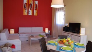 Un salon avec un canapé, une table à manger dressée avec des assiettes et des verres, et un téléviseur posé sur un meuble.