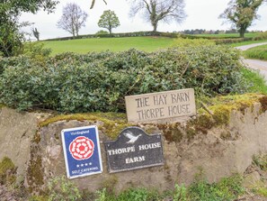 Ländliche Umgebung mit Schildern für 'The Hay Barn Thorpe House' und 'Thorpe House Farm', die eine Selbstversorgerunterkunft kennzeichnen.