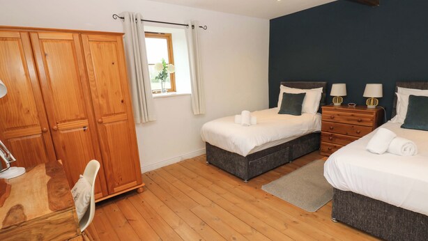 A room with two beds, a wooden wardrobe, a desk, and a window with curtains. - The Hay Barn (Ripon)
