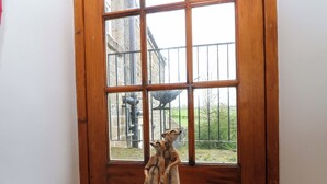 A room with a large wooden-framed window, a concrete floor, and a view of a building and trees outside. - The Hay Barn (Ripon)