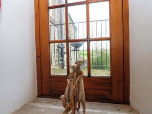 A room with a large wooden-framed window, a concrete floor, and a view of a building and trees outside. - The Hay Barn (Ripon)
