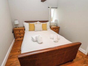 Ein ordentlich bezogenes Bett mit weißen Bettwäsche und zwei Handtüchern, ein Nachttisch aus Holz mit einer Lampe und eine Kommode mit Schubladen.