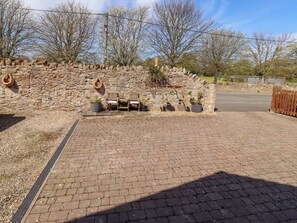 A paved area with stone walls, a wooden bench, and potted plants. - Willow Cottage (Seahouses)