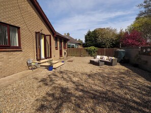 A brick house with a patio area, a sofa, and a small table. - Willow Cottage (Seahouses)
