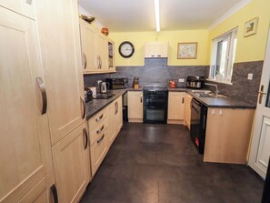 A compact kitchen with wooden cabinets, a black oven, a microwave, and a sink. - Willow Cottage (Seahouses)