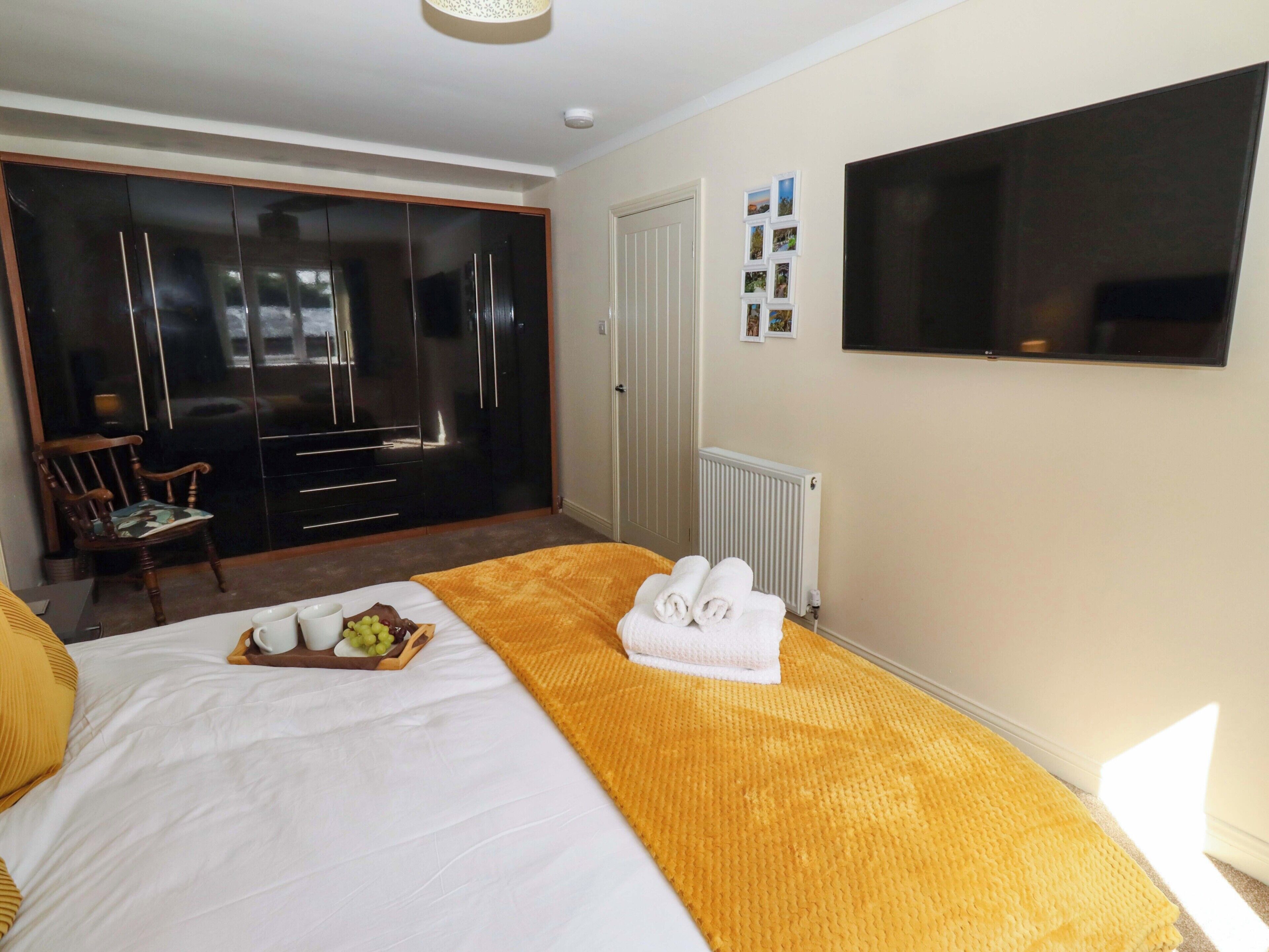 A hotel room with a bed, a wardrobe, a television, and a small table with fruits and towels.