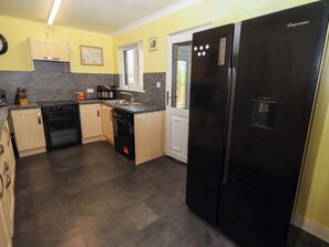 A kitchen with a black refrigerator, a dishwasher, an oven, and a coffee maker. - Willow Cottage (Seahouses)