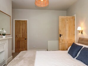 A bedroom with a bed, a wooden door, a radiator, and a wall-mounted lamp. - Kents Cottage (Torquay)