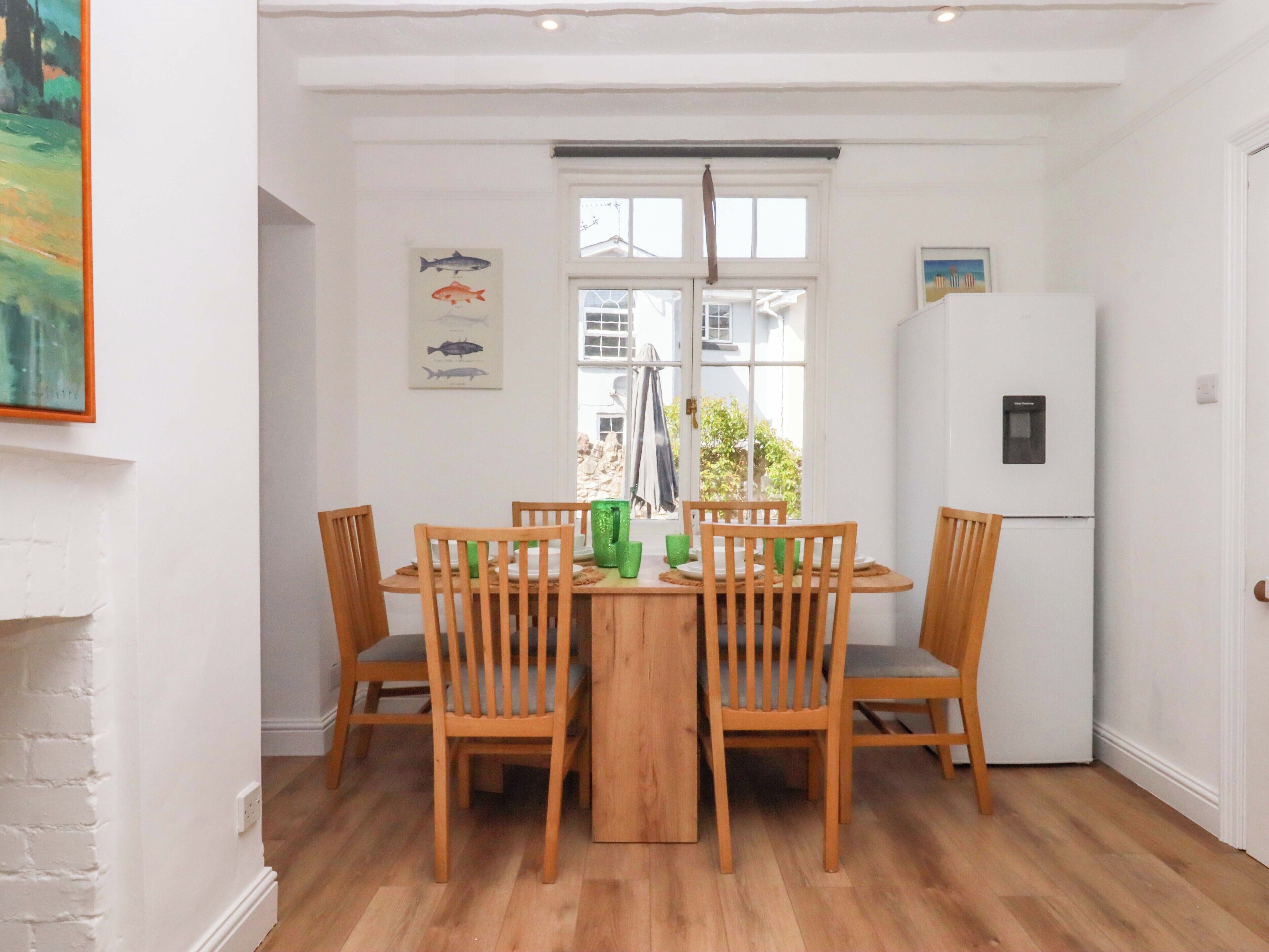 A dining area with a wooden table and chairs, a window with a view, a refrigerator, and a wall-mounted fish illustration.