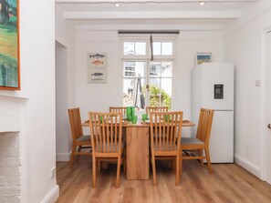 A dining area with a wooden table and chairs, a window with a view, a refrigerator, and a wall-mounted fish illustration. - Kents Cottage (Torquay)