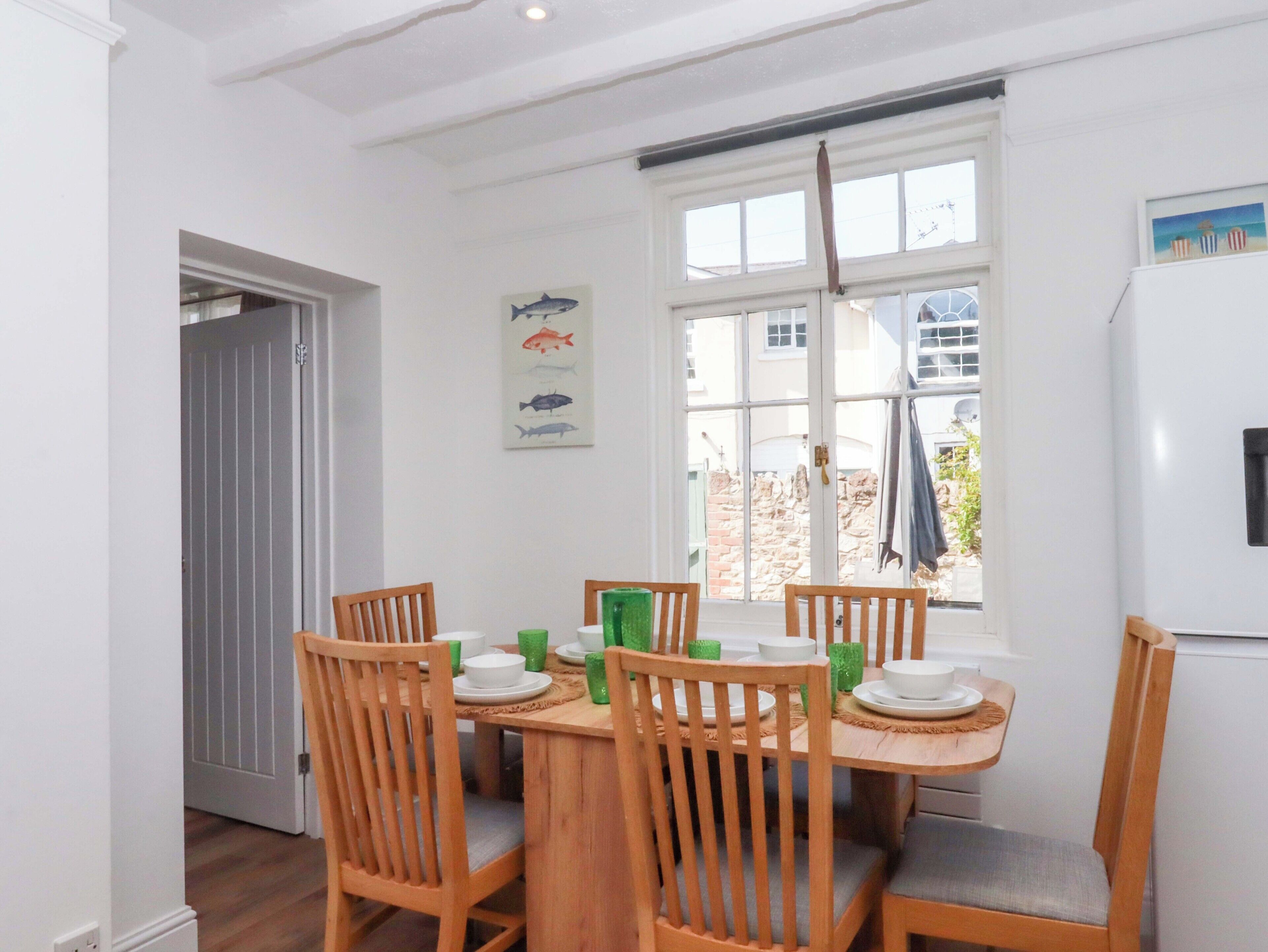 A dining area with a wooden table and chairs, a fish-themed wall hanging, and a view through a window.