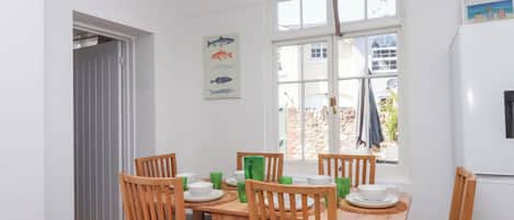 A dining area with a wooden table and chairs, a fish-themed wall hanging, and a view through a window.