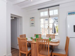 Ein Essbereich mit Holztisch und Stühlen, einem Wandbehang mit Fischmotiv und Blick durch ein Fenster.